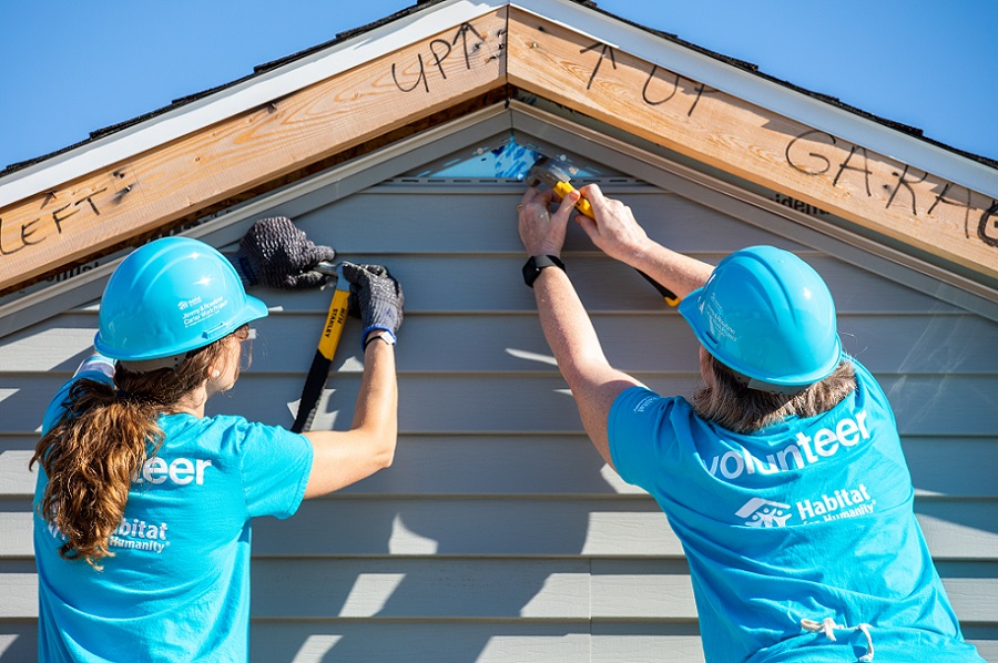 Two women volunteer on a construction site. This image shows them nailing in part of the roof.
